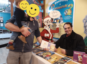 L'auteur Bruno Bertin en dédicace avec un papa et son fils devant la table de livres.