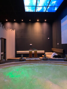 Rebord de jacuzzi avec apéritifs et lumières tamisées, écrans au plafond qui diffusent des images de poissons et de fonds marins.