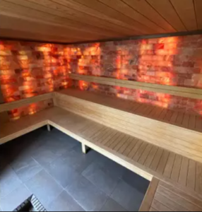 Idée Saint-Valentin : l'Espace Nordique du centre aquatique les Ondines à Janzé. Hamamm et grotte de sel, bancs en bois et lumière tamisée orangée.